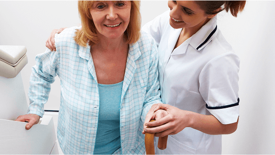 Lady climbing stairs with a walking stick and being helped by a healthcare professional  image