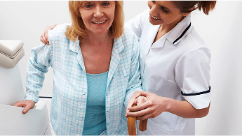 Lady climbing stairs with a walking stick and being helped by a healthcare professional  image
