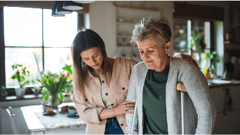 Woman on crutches being helped walk across a kitchen by another woman image