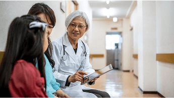Healthcare professional sat down talking to a child and guardian in a hospital corridor image