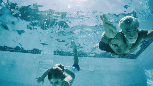 Older man and boy swimming underwater in a pool image