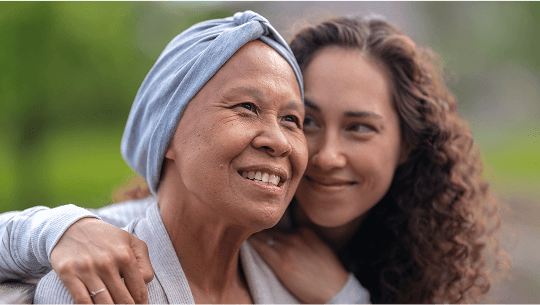 Woman sat outside with a headscarf on and being hugged from the side by another woman image