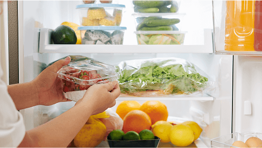 Person putting strawberries into a fridge full of other healthy food image