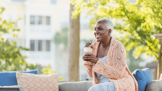 Woman sat outside on garden furniture, drinking a smoothie image