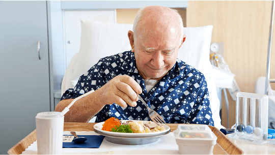 Elderly man smiling and eating a meal in a hospital bed image