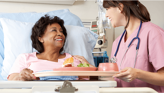 Woman in hospital bed being served a meal by a healthcare professional image