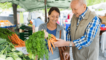 Man and woman at a food market looking at a bunch of carrots image