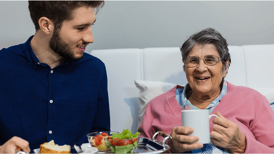 Man with serving tray of food for elderly lady sat down image