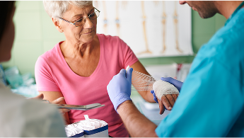 Elderly woman having her hand bandaged up by a healthcare professional image