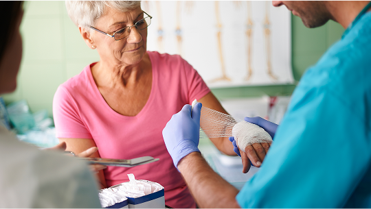 Elderly woman having her hand bandaged up by a healthcare professional image