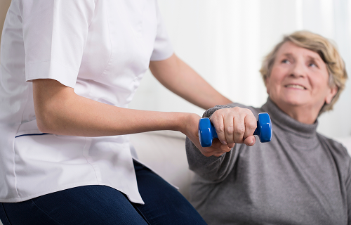 Lady being helped by a healthcare professional to do light dumbell exercises image