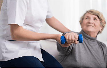 Lady being helped by a healthcare professional to do light dumbell exercises image