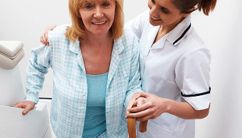 Lady climbing stairs with a walking stick and being helped by a healthcare professional  image