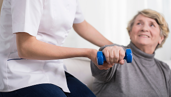Lady being helped by a healthcare professional to do light dumbell exercises image
