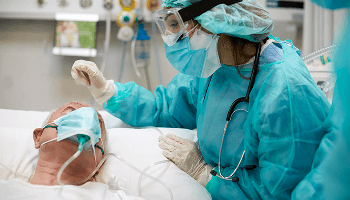 Elderly man wearing a mask in a hospital bed being examined by a healthcare professional wearing PPE image