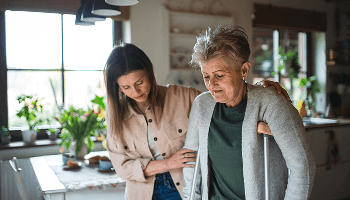 Woman on crutches being helped walk across a kitchen by another woman image