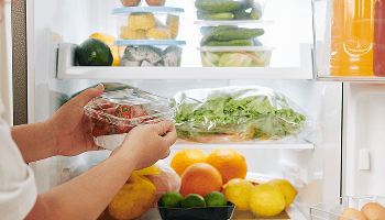 Person putting strawberries into a fridge full of other healthy food image