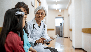 Healthcare professional sat down talking to a child and guardian in a hospital corridor image