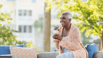 Woman sat outside on garden furniture, drinking a smoothie image