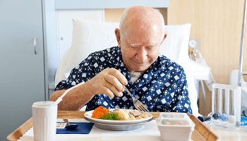 Elderly man smiling and eating a meal in a hospital bed image