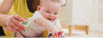 Baby with a woman on the floor, playing with wooden blocks together image