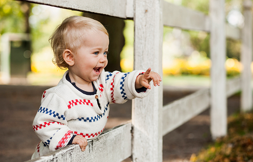 Child outside and by a wooden fence, smiling and pointing image