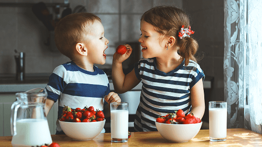 Girl feeding a boy a strawberry at a kitchen table image