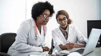 Two healthcare professionals sat at a desk, looking at a laptop screen image