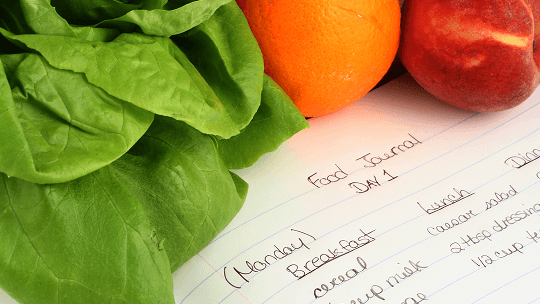 Notepad with food diary information within it, next to healthy foods image