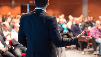 A man stood at the front of a lecture hall giving a talk to a room full of people image