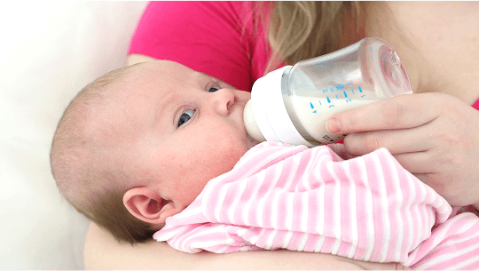 Baby being fed using a baby bottle image
