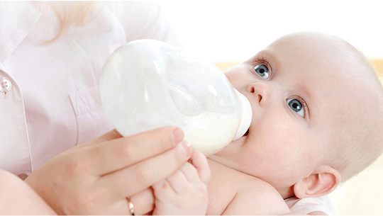 Baby being fed using a baby bottle image