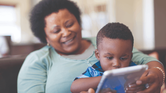 Child using a tablet device whilst sat on a woman's lap image
