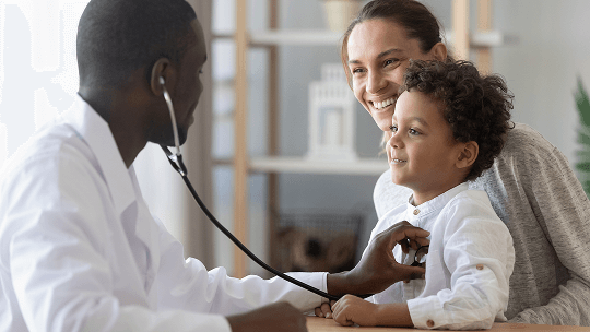 Child sat on a woman's lap, being examined by a healthcare professional using a stethoscope image