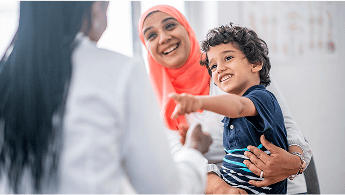 Child smiling and pointing at healthcare professional, whilst being held by a woman image