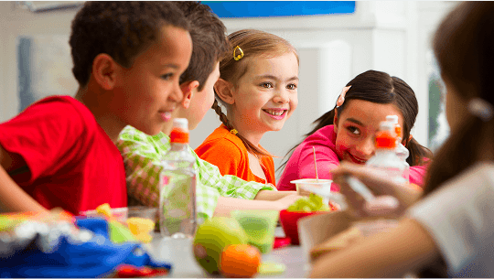 Group of children looking happy whilst eating around a table image