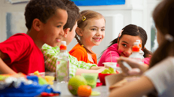 Group of children looking happy whilst eating around a table image