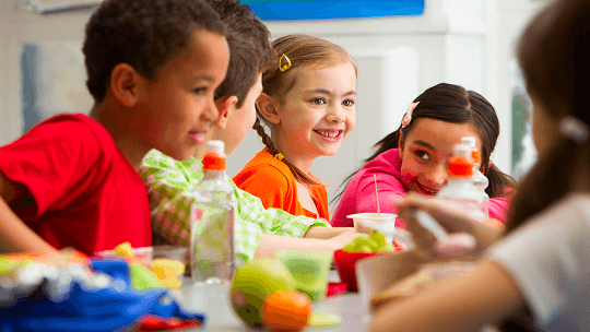 Group of children looking happy whilst eating around a table image