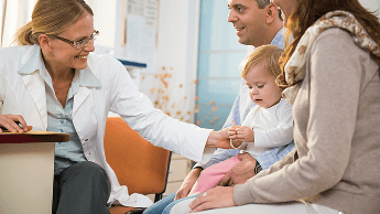 Infant being held by parents in a consultation office with the doctor smiling at the child image