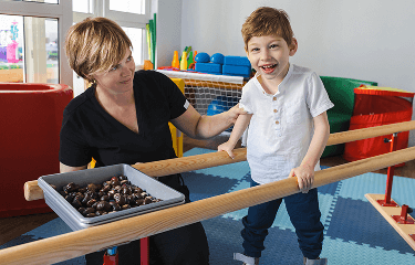 Boy next to his carer, learning to walk using parallel walking bars image