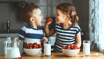 Girl feeding a boy a strawberry at a kitchen table image