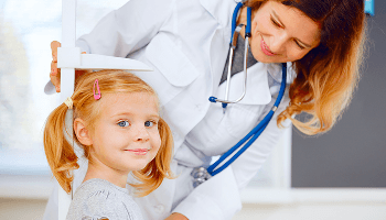 Child smiling whilst having her height measured by a healthcare professional image