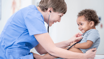 Healthcare professional examining a young, smiling child with a stethoscope image