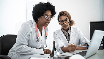Two healthcare professionals sat at a desk, looking at a laptop screen image