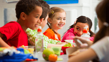 Group of children looking happy whilst eating around a table image