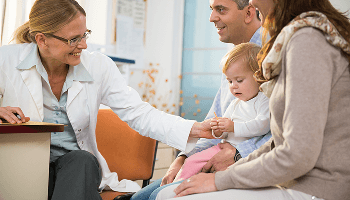 Infant being held by parents in a consultation office with the doctor smiling at the child image