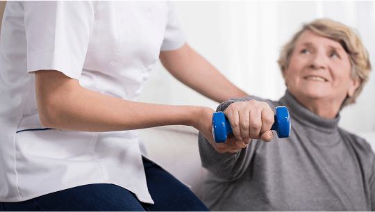 Lady being helped by a healthcare professional to do light dumbell exercises image